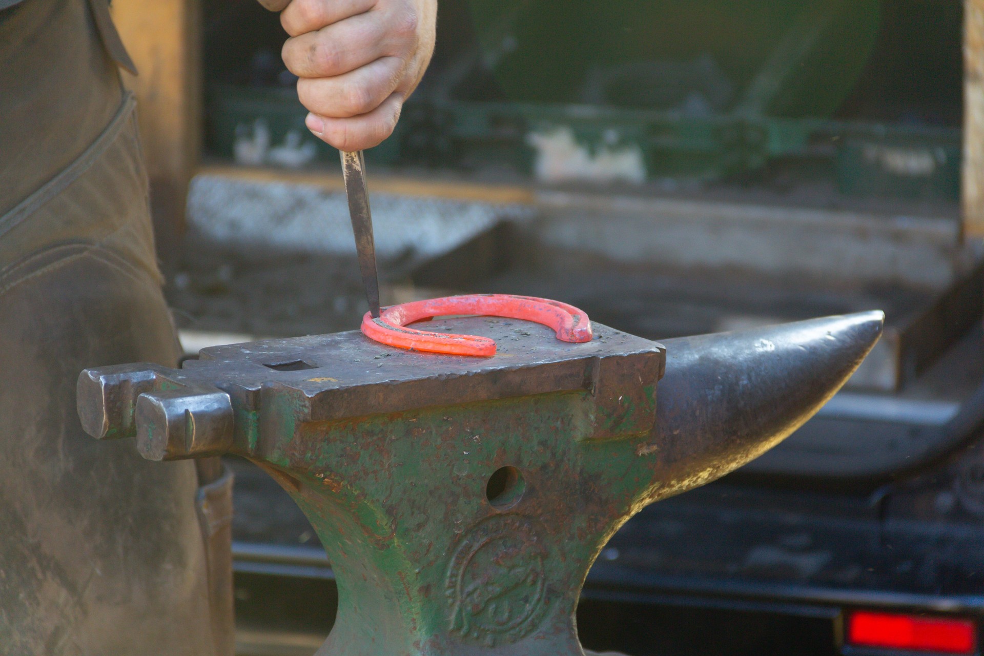 Close up shot of red hot metal horse shoe on anvil as farrier blacksmith works on it to shape it to fit the horses foot.